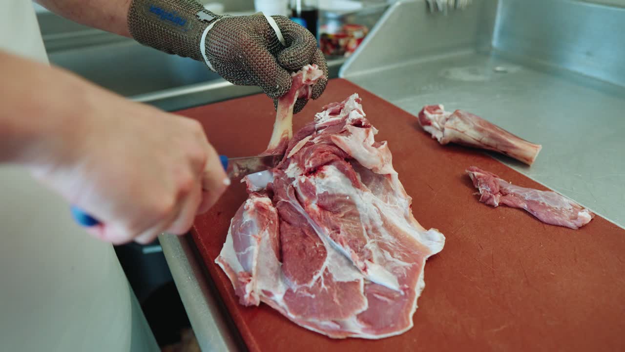 macellaio che taglia con cura il grasso della carne di agnello cruda sul banco da lavoro indossando un guanto da macellaio