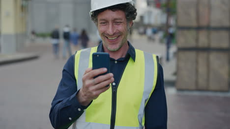 Porträt-Eines-Glücklichen-Bauarbeiters,-Der-Smartphone-Video-Chats-Nutzt,-Winkender-Handingenieur,-Der-Auf-Dem-Mobiltelefon-Spricht-Und-Einen-Schutzhelm-Mit-Reflektierender-Kleidung-In-Zeitlupe-In-Der-Stadt-Trägt