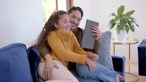 Feliz-Madre-E-Hija-Birraciales-Abrazándose-En-El-Sofá-Y-Usando-Una-Tableta-En-La-Soleada-Sala-De-Estar