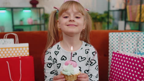 young children girl with lots of gifts celebrating birthday party making a wish, blowing cake candle