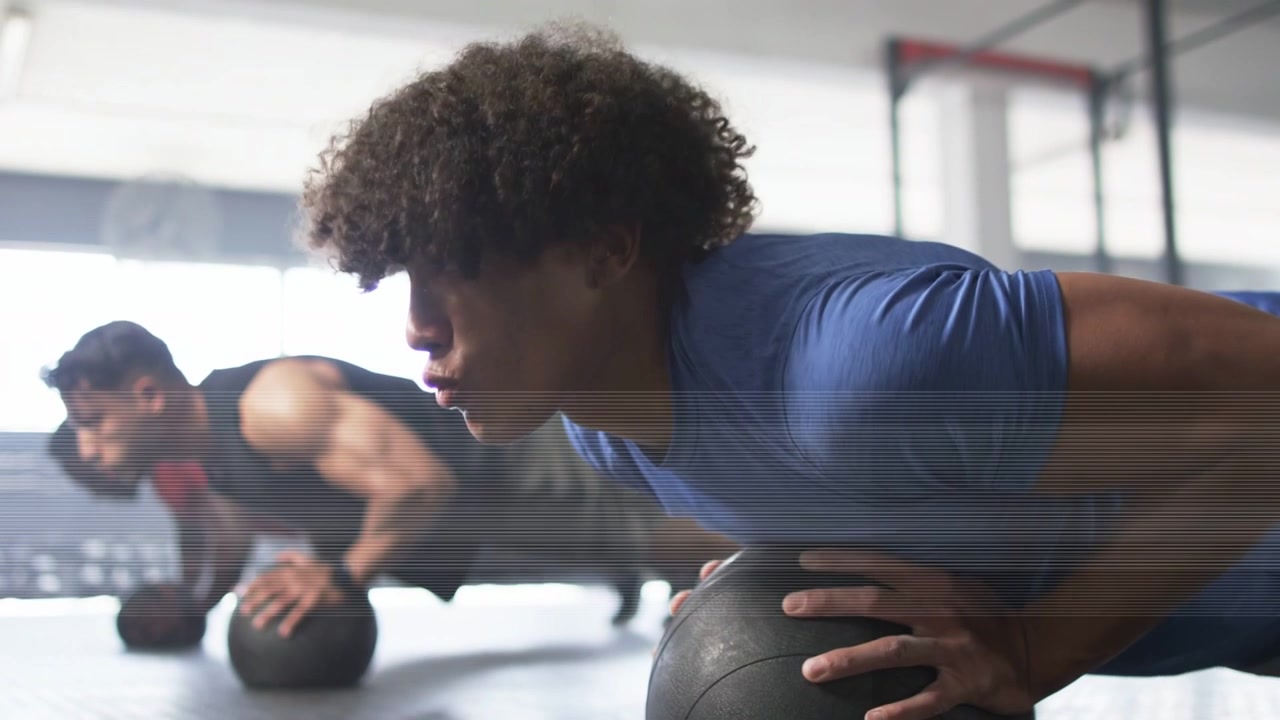 Partners doing fitness pushups in gym gripping 15 lb med ball, lowering then pressing for strength