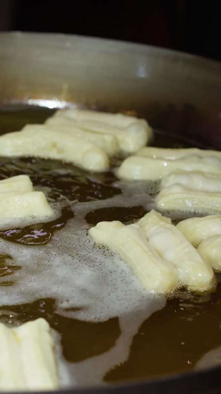 Close-up of traditional Chinese dough sticks frying in bubbling hot oil within a large wok.