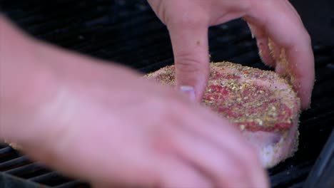 two hands put a thick raw rib eye steak on a grill starting its grilling process in slow motion