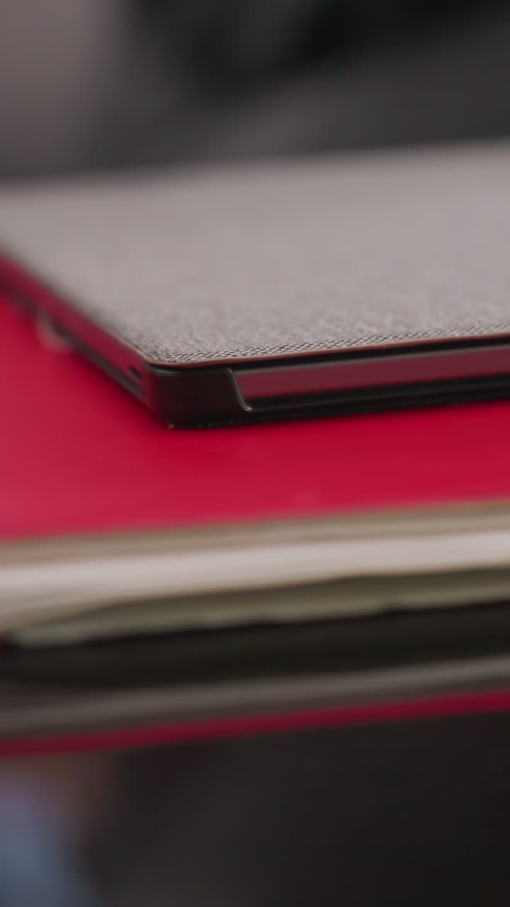 Close-up of gray laptop placed on red notebooks and papers on glass desk. Organized workspace in corporate office, focusing on productivity tools for business and career management