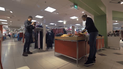 man with mobile shooting woman choosing kids clothing in the store