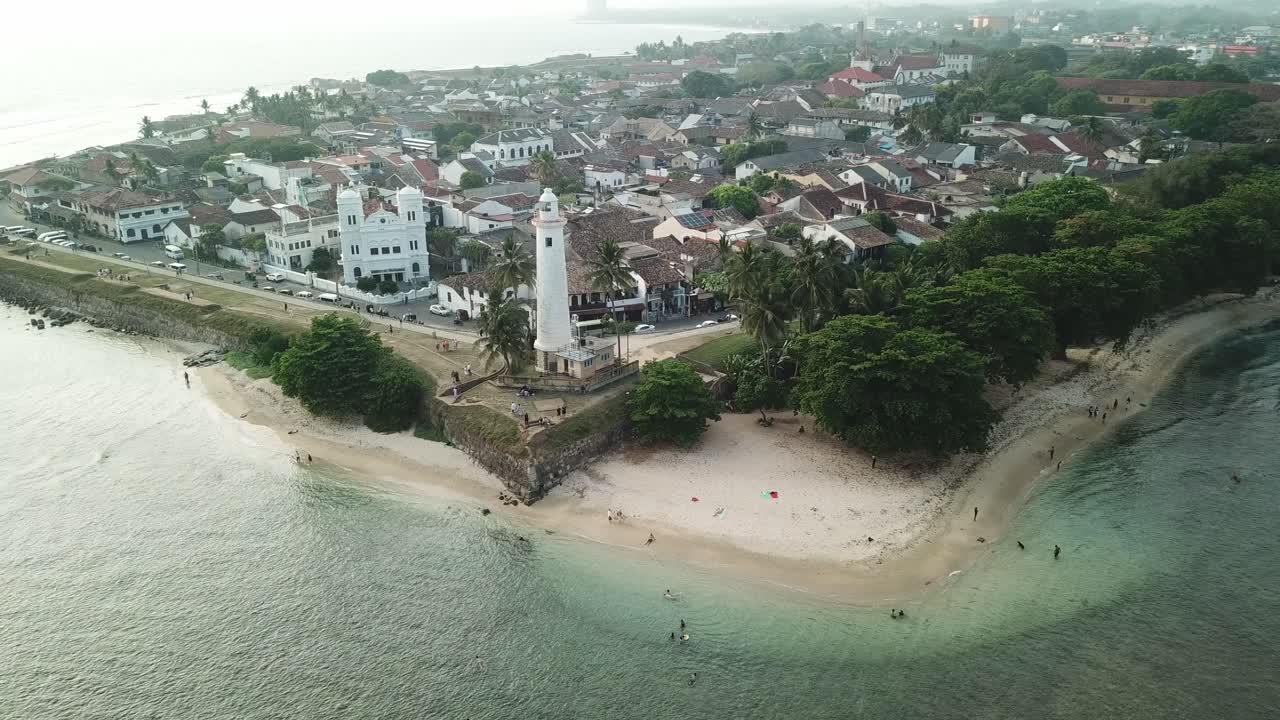 Drone footage captures the tranquil beach and the Galle lighthouse, surrounded by swaying palm trees and crystal-clear waters of the Indian Ocean. A perfect tropical getaway.
