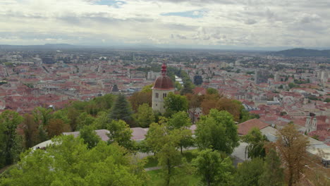 vista de la órbita aérea volando alrededor de la histórica torre glokenturm en el parque arbolado de la colina schloßberg de graz