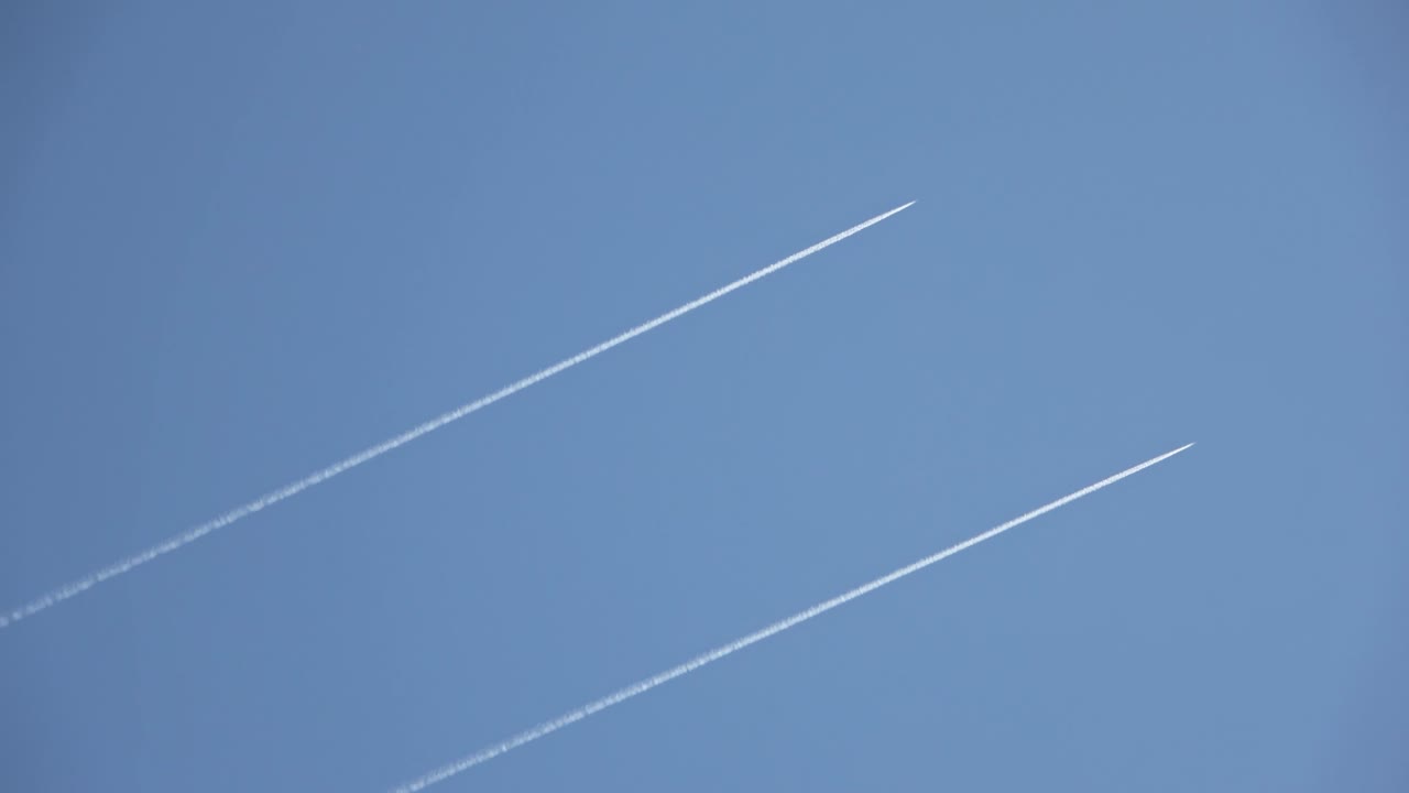 Two military jets and an airliner flying high in the sky leaving contrails in the clear blue sky.