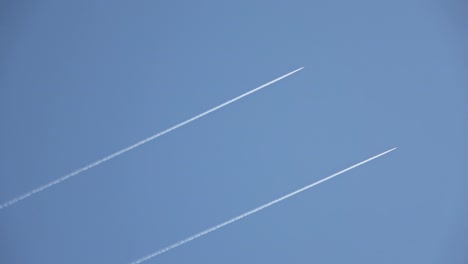 two military jets and an airliner flying high in the sky leaving contrails in the clear blue sky.