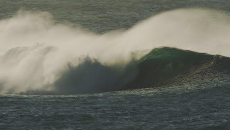 dark ocean wave rolls in under cloudy sunset sky with glowing edge mist in slow motion