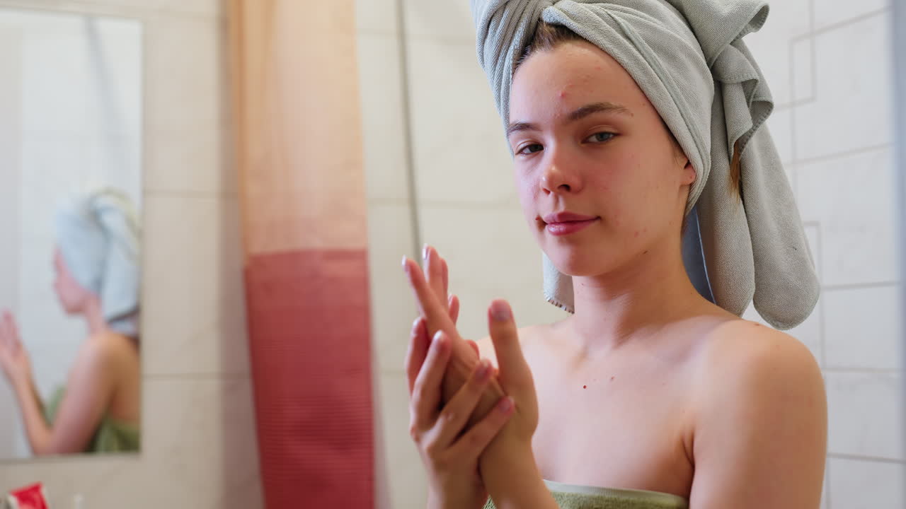 Close-up view of young lady wrapped in light green towel, sitting in bathroom, rubbing hands together with mirror reflection, fresh-faced, preparing skincare, morning routine, wellness moment