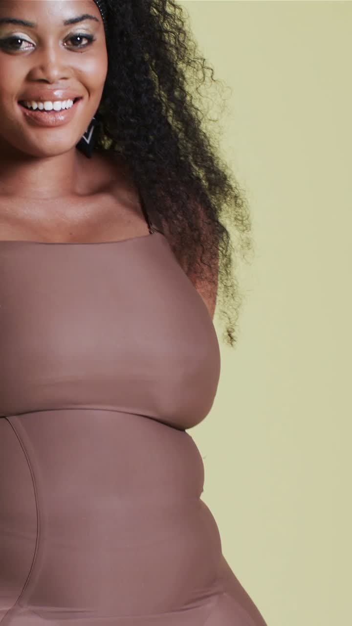 Video verticale: La telecamera si alza, una modella sistema l'intimo modellante marrone, posa in studio mostrando la vestibilità.