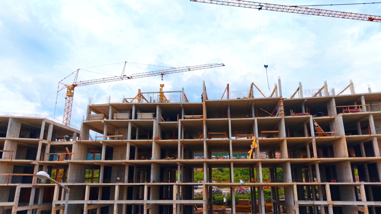 Low angle view of massive concrete building structure frame. Look up view of reinforced concrete framework under construction with yellow crane under cloudy sky.