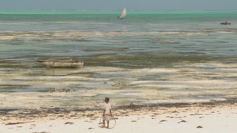 Ein-Mädchen-Steht-Mit-Einem-Spielzeugring-Am-Strand-Und-Blickt-Auf-Ein-Fernes-Segelboot