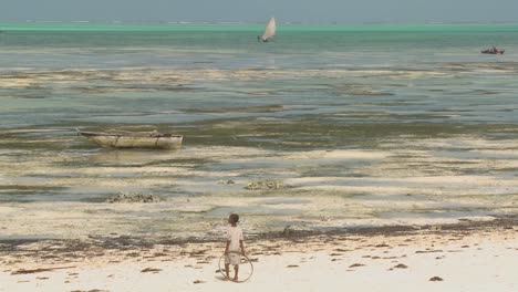 una niña se para con un anillo de juguete en la playa mirando un velero distante