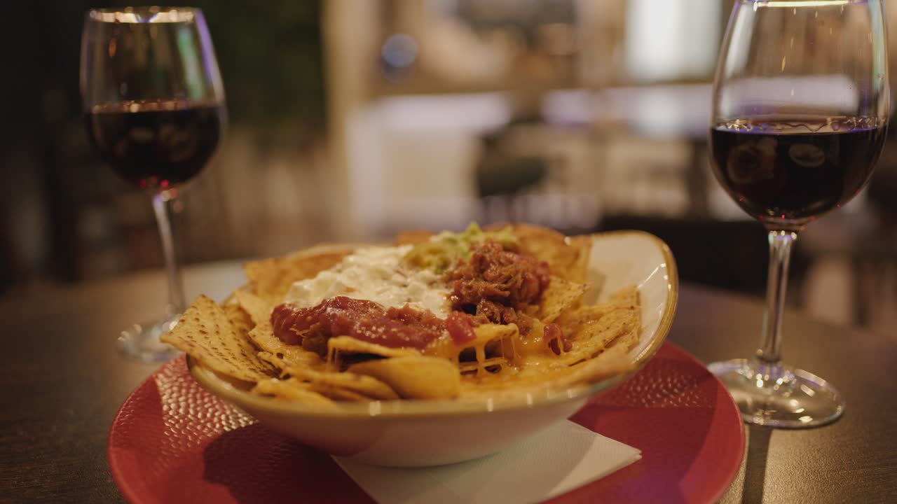 Hand uses fork and knife to eat nachos with dip in a cozy restaurant