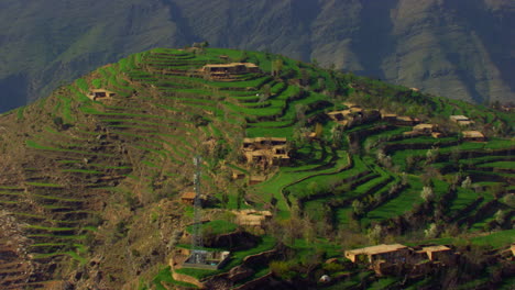 A-beautiful-drone-drive-over-the-green-mountain-crossing-the-houses-and-a-satellite-tower,-Other-beautiful-mountains-in-the-background