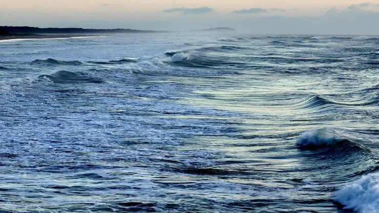 Aerial view of the foamy waves crashing against the shoreline, Sunlight casting a golden glow on the ocean's froth