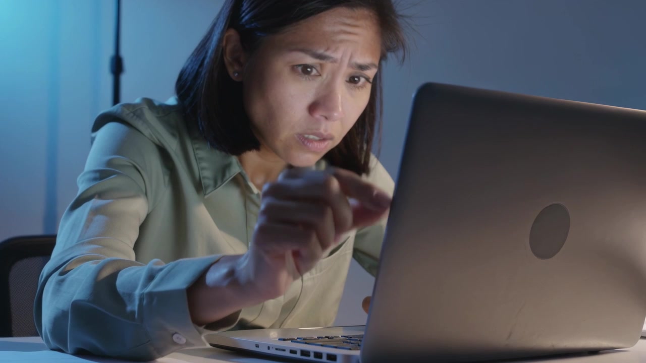 Leaning woman in light green shirt touching laptop after alert at desk, with papers and lamp