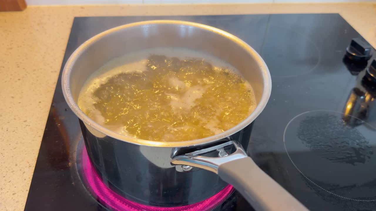 Close-up static shot of pasta cooking in bubbling water on a glowing induction stovetop
