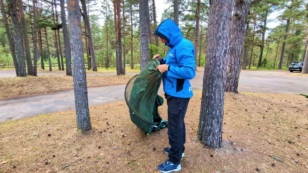 A Man Preparing to Set up His Camping Tent in a Wooded Park - Medium Shot