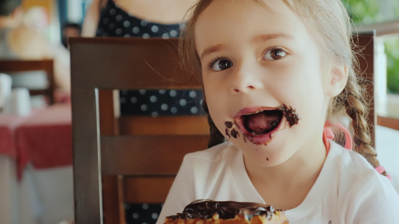 una niña genial está comiendo un bollo dulce, su cara está manchada de chocolate