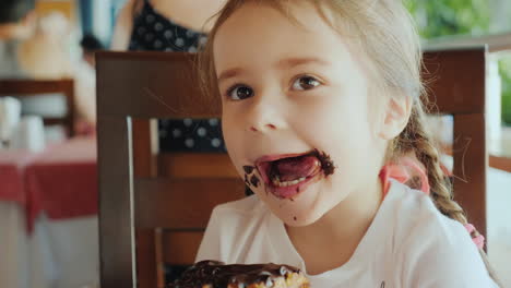 una niña genial está comiendo un bollo dulce, su cara está manchada de chocolate