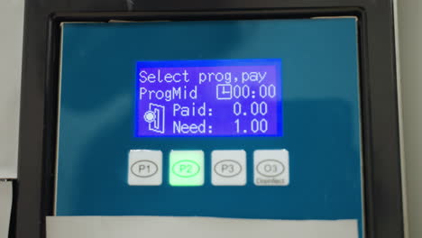 close zoom on control panel buttons of industrial laundry washer, showcasing display and settings as camera pushes toward interface; stainless rim and glass door visible, clean laundromat equipment