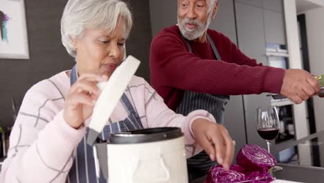 senior biracial couple cooking dinner and cleaning waste in kitchen, unaltered, in slow motion