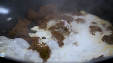 verter leche de coco blanca en una sartén negra muy caliente con pasta seca de curry marrón tailandés