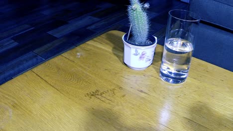 un hombre europeo con guante negro recoge un arma de fuego negra cargada de una mesa de roble junto a un vaso con líquido