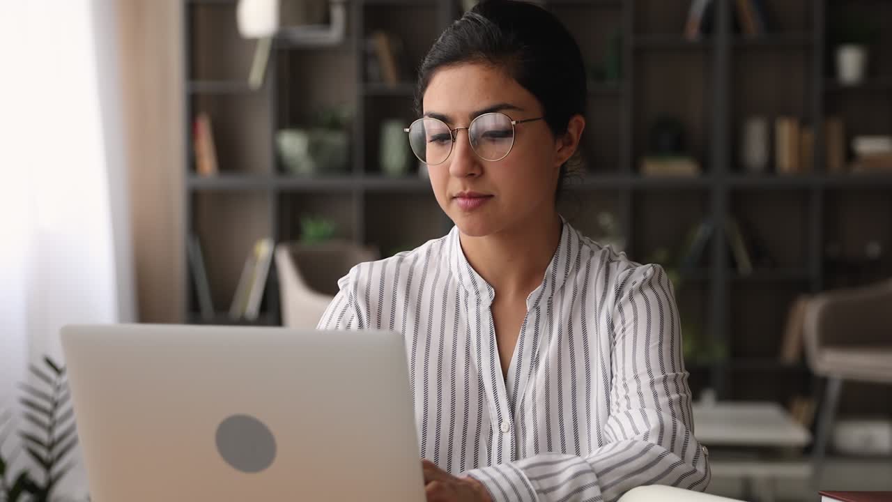 Happy young indian ethnicity woman in eyeglasses working on computer.