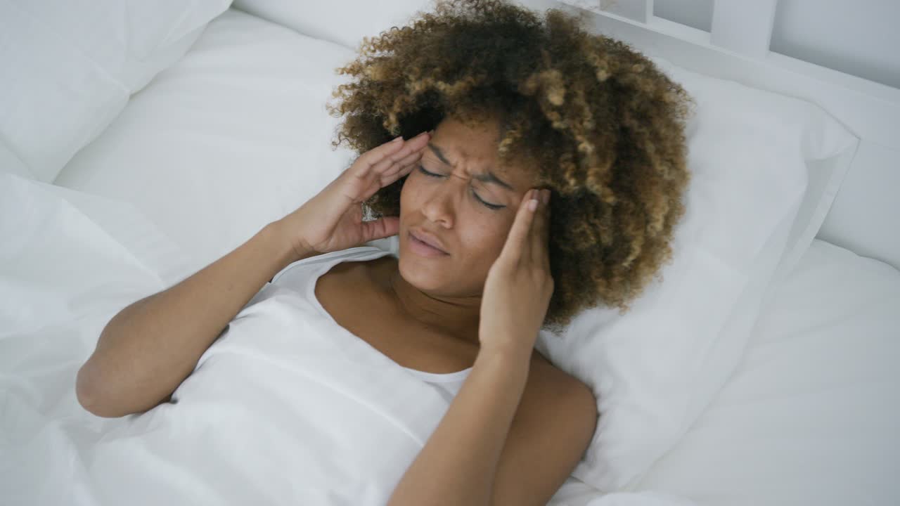 mujer joven que tiene dolor de cabeza acostado en la cama