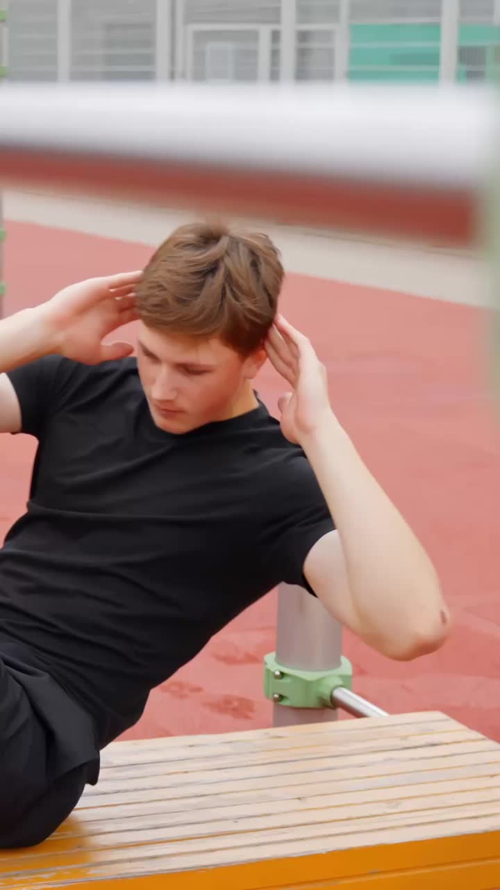 Athletic young man performs twisting crunch exercises on running track during outdoor fitness workout