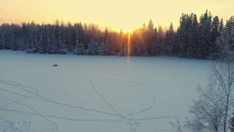 aerial drone ascending flyback over wooden house in winter landscape and snowy forest at sunset