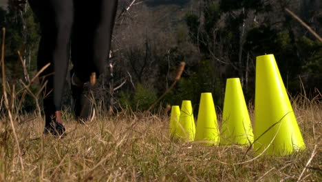 sección baja de una mujer corriendo a través de conos de entrenamiento