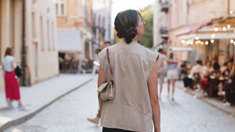 rear view of young woman tourist walking through the street outdoors looking searching for a way