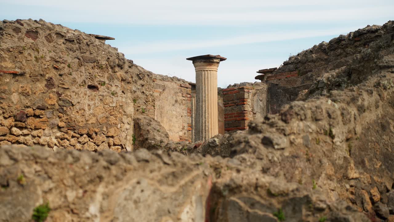 Vista attraverso le rovine stratificate di Pompei con una colonna romana scanalata in piedi, incorniciata da muri in pietra e mattoni consumati dal tempo all'interno dell'antico sito archeologico.