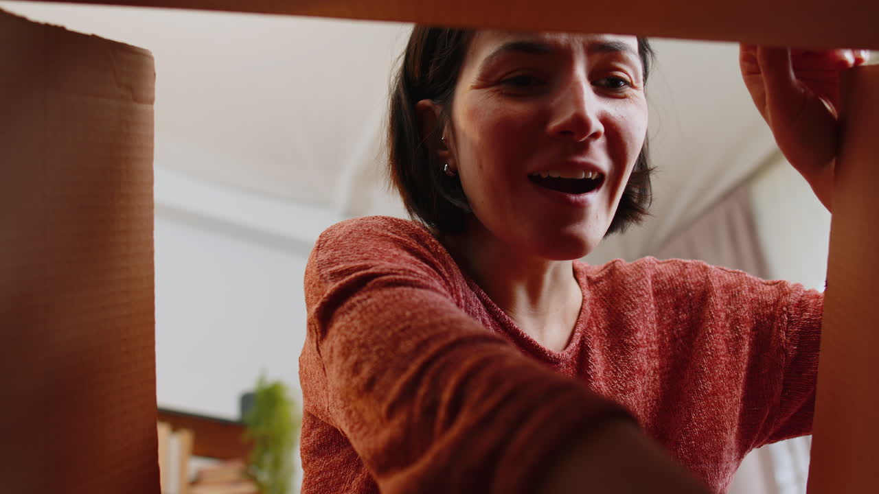 directamente debajo del retrato mujer abriendo una caja de cartón desempaquetando la entrega del producto aplaudiendo emoción