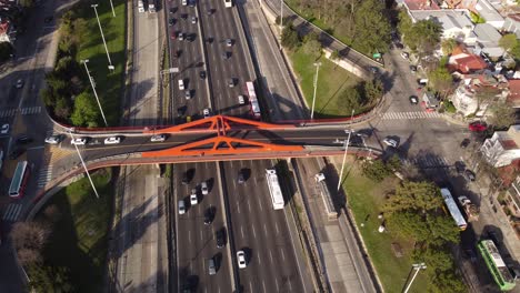 aerial top down shot of cars driving on pan-american highway under red bridge in buenos aires