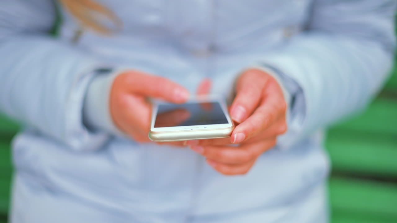 Donna con giacca blu che scorre il telefono seduta su una panchina verde nel parco