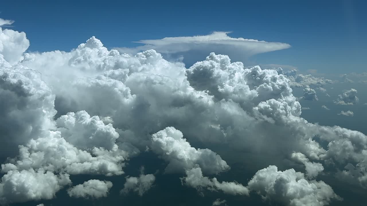 An skyscape view from a jet cockpit flying above massive and dangerous cumulonimbus storm clouds, under blue color sky. Ultra-realistic 4K