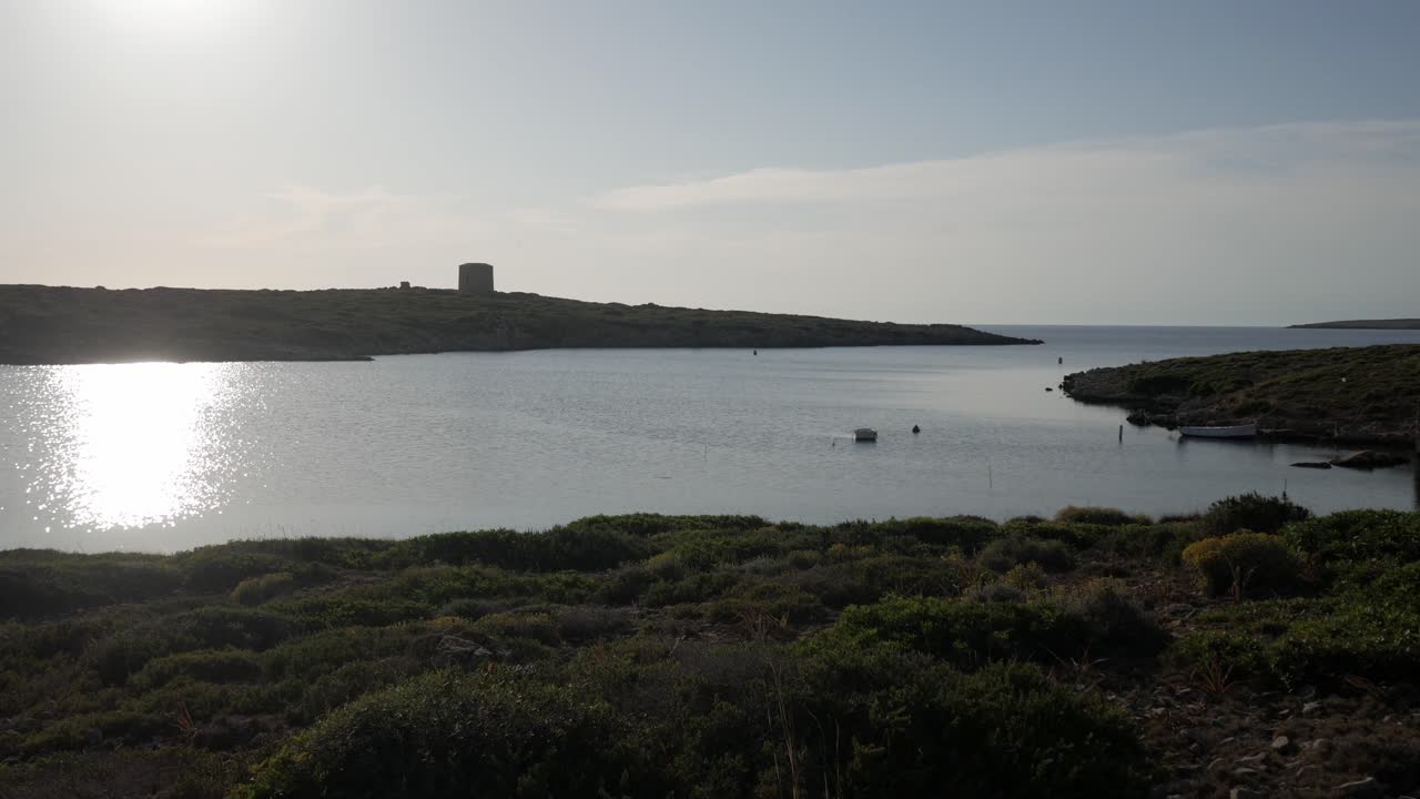 Poklidná pobřežní scéna u Torre De Sanitja, Puerto De Sanitja, s klidnými vodami a záři západu slunce.