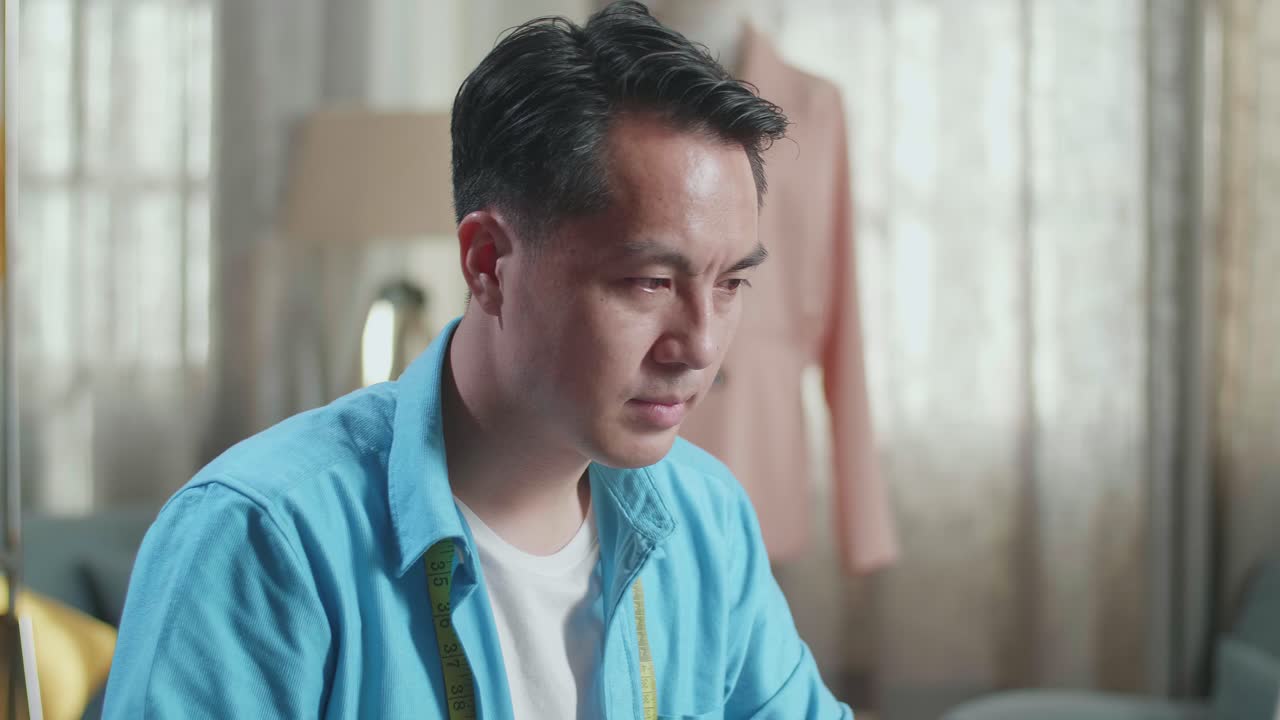 스튜디오에서 옷을 디자인하는 동안 노트북을 사용하고 커피를 마시는 아시아 남성 디자이너의 클로즈업