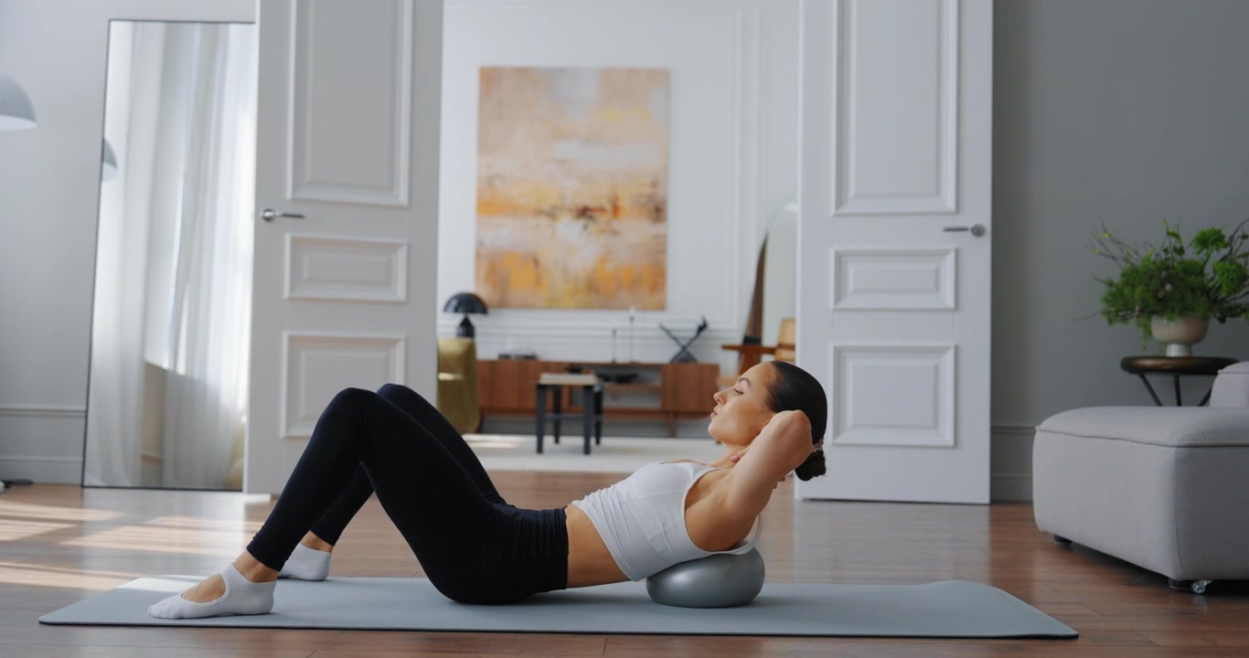 Giovane donna che esegue esercizi per il core con una palla Pilates a casa