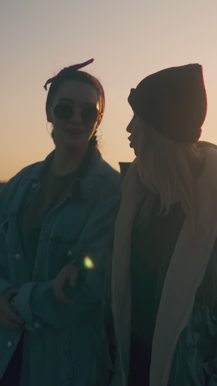 group of smiling girl and guy tourists walk along field to modern campsite in calm autumn evening at back sunset