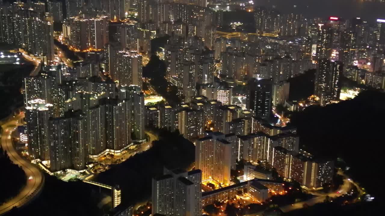 A breathtaking drone view of Hong Kong at night, showcasing the glowing skyline, busy harbor, and vibrant city lights from above.