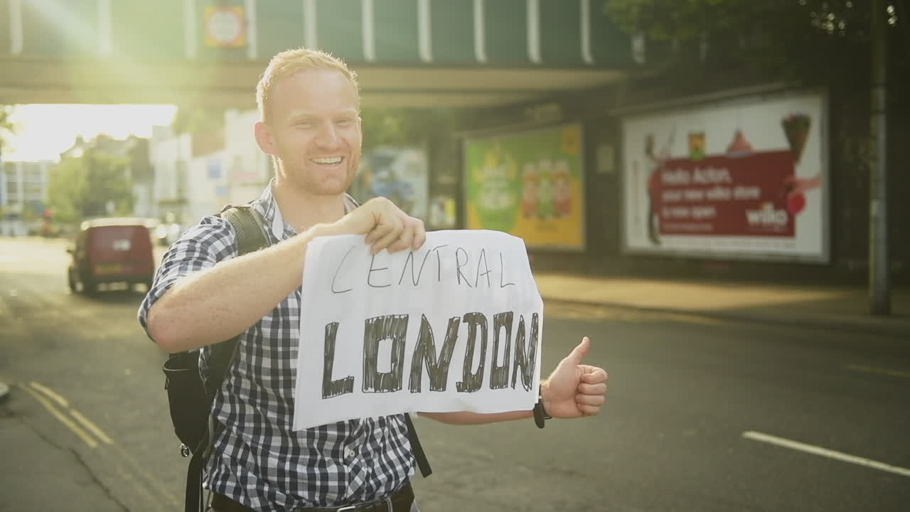 Time lapse of a man holding up his thumb for hitchhiking in London, back view, static shot