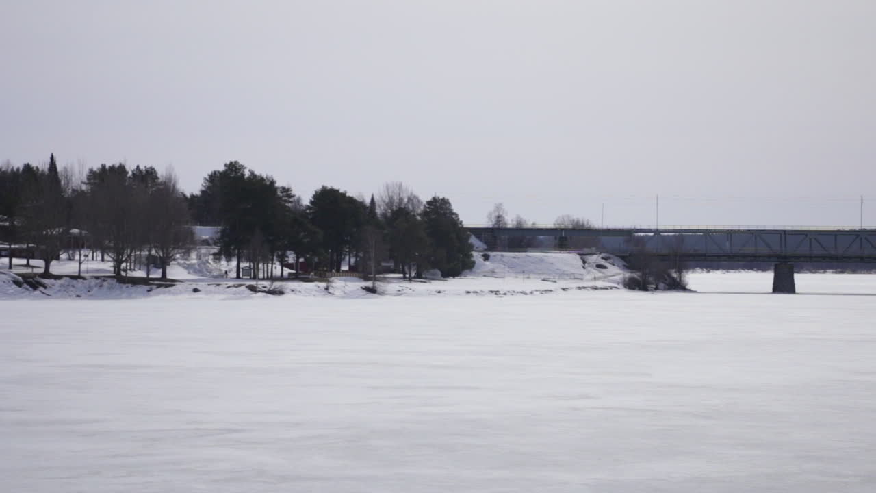 paisaje nevado con árboles y un puente lejano sobre un río congelado en rovaniemi, finlandia día nublado de invierno