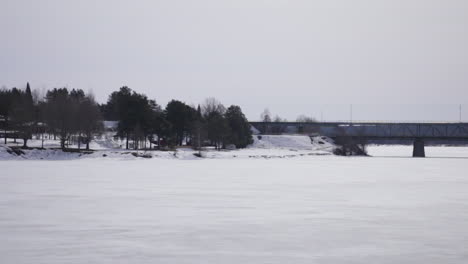 snowy landscape with trees and a distant bridge over a frozen river in rovaniemi, finland cloudy winter day